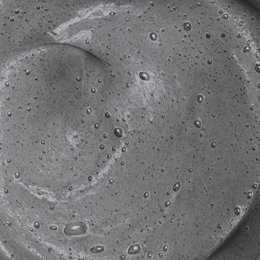 Botanical liquid facial cleanser with activated charcoal and tea tree in amber glass bottle on walnut surface.