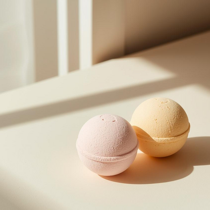 Two bath bombs, one pink and one beige, on a light surface with soft shadows.
