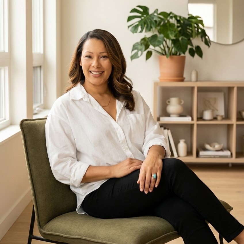 Woman sitting on a chair in a room with a plant and shelves in the background
