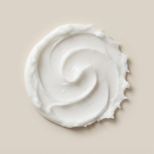 A swirl of thick, creamy white lotion or body butter on a solid beige background.