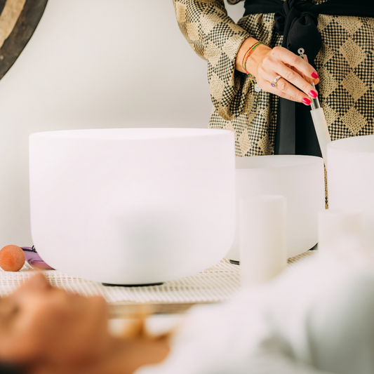 Sound bath meditation session featuring white frosted crystal singing bowl played near a resting client in a calming wellness environment.
