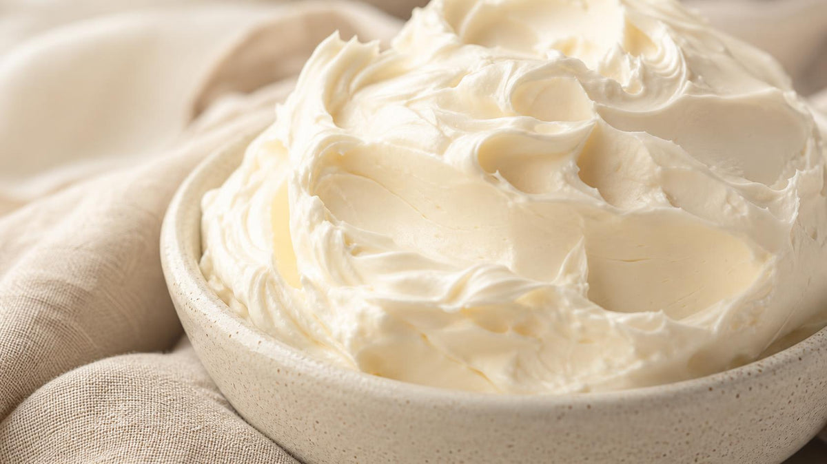 Close-up of whipped ivory body butter with soft peaks in a shallow ceramic dish on unbleached linen — PureButterMelts